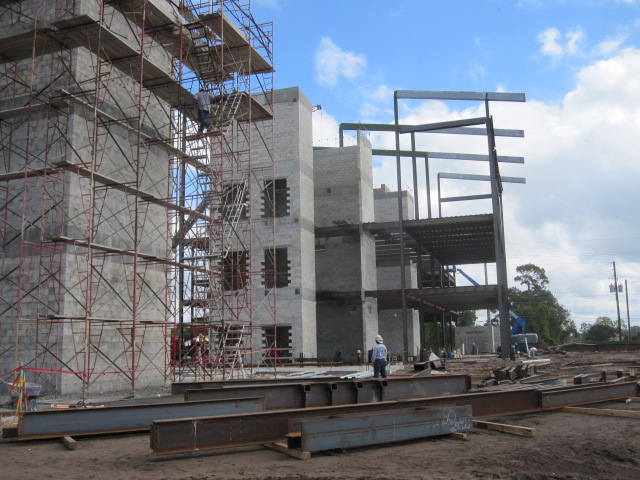 Large concrete pillars under construction with one man wearing a blue shirt and white construction helmet looking at the structure